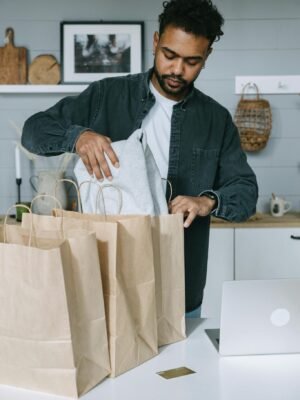 Adult man organizing purchases with paper bags and laptop in a modern home setting.