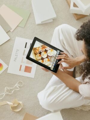 Woman using tablet surrounded by design tools and gift box, showcasing creativity and online work.